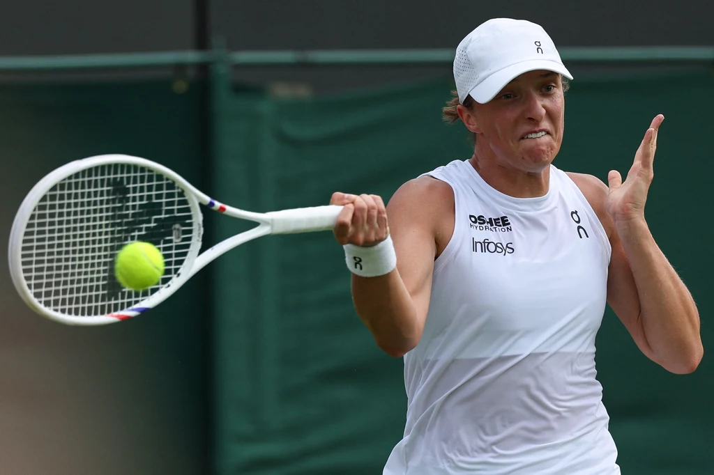 Iga Świątek rywalizowała z Poliną Kudiermietową w pierwszej rundzie Wimbledonu Tenisistka w białym stroju i czapce wykonuje uderzenie forhendowe podczas meczu na korcie tenisowym.
