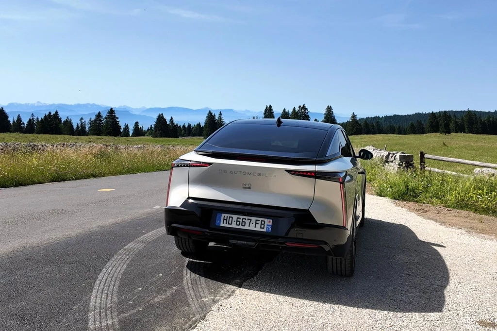 Katalogowe ceny DS N8 startują od 249 tys. zł. Srebrny samochód elektryczny DS Automobiles zaparkowany przy bocznej drodze wśród zielonych łąk, w tle górzysty krajobraz i linia lasu, wyraźna tablica rejestracyjna pojazdu, ślady opon na asfalcie.