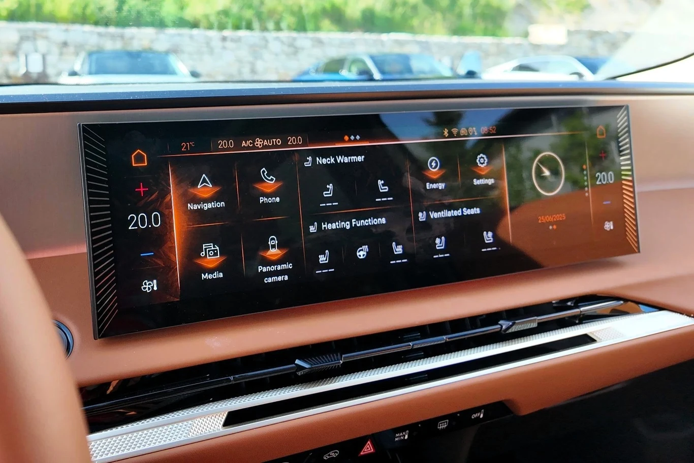 Duży panoramiczny ekran dotykowy w nowoczesnym samochodzie, pokazujący menu z wieloma funkcjami, w tym nawigacją, telefonem, mediami, kamerą panoramiczną, ustawieniami siedzeń i klimatyzacją, z przejrzystą grafiką i intuicyjnym układem ikon.