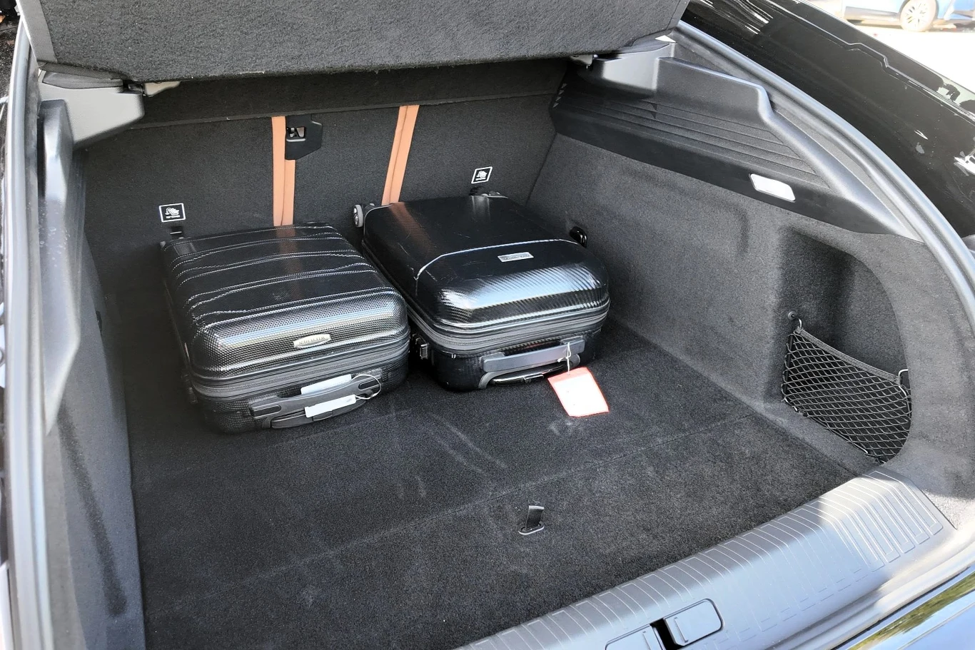 Dwie czarne walizki mieszczące się w dużym, czystym bagażniku samochodu, wyposażonym w schowki po bokach oraz matę ochronną na podłodze.