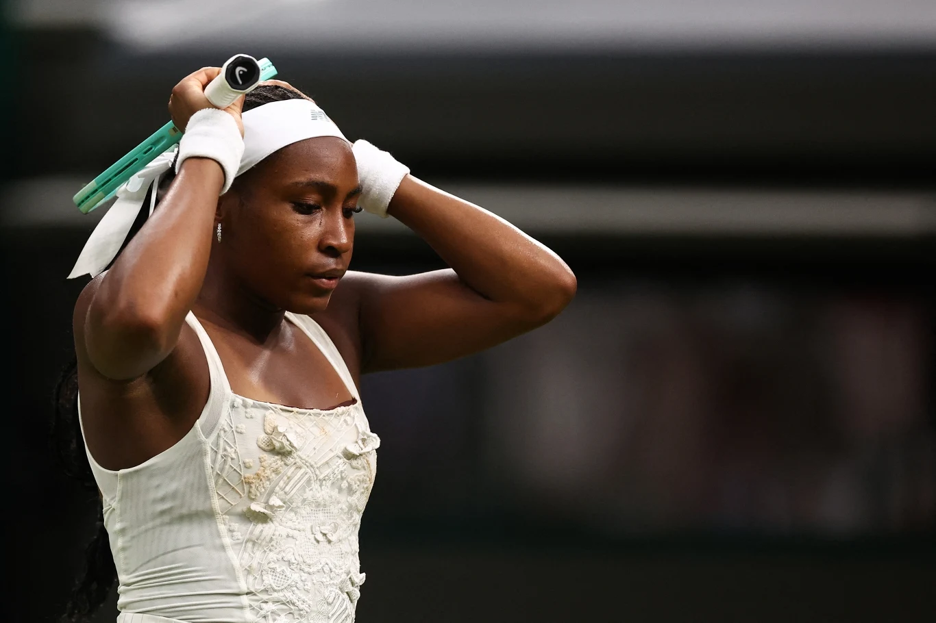Coco Gauff rywalizowała z Dajaną Jastremską w pierwszej rundzie Wimbledonu Tenisistka w białym stroju sportowym poprawia opaskę na głowie, trzymając rakietę tenisową, wyrażając koncentrację i determinację.