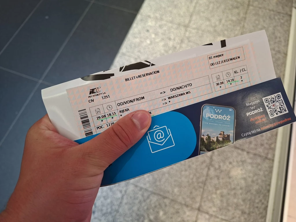 Bilet kolejowy PKP Intercity trzymany w dłoni, wraz z ulotką promocyjną dotyczącą podróży. Bilet zawiera szczegóły dotyczące trasy i rezerwacji miejsca, a w tle widoczna jest podłoga z kafelków.