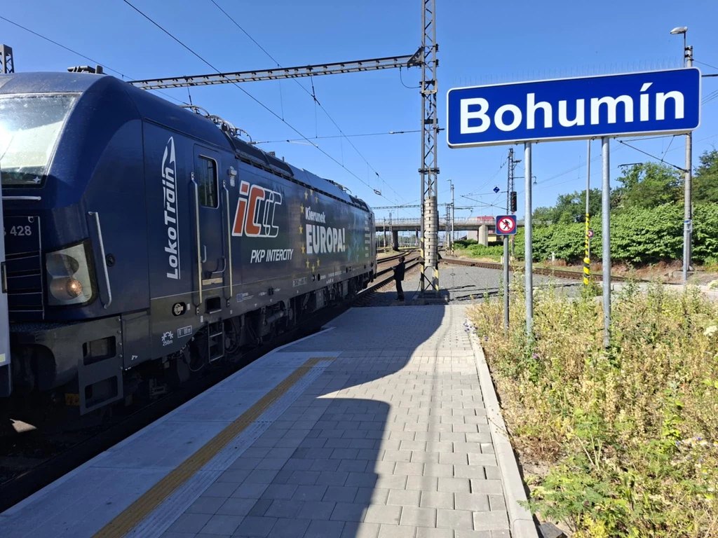 Nowoczesna lokomotywa z logo IC PKP Intercity stoi na peronie stacji kolejowej Bohumín, obok widoczny jest niebieski znak z nazwą miejscowości, wokół torów roślinność i elementy infrastruktury kolejowej.