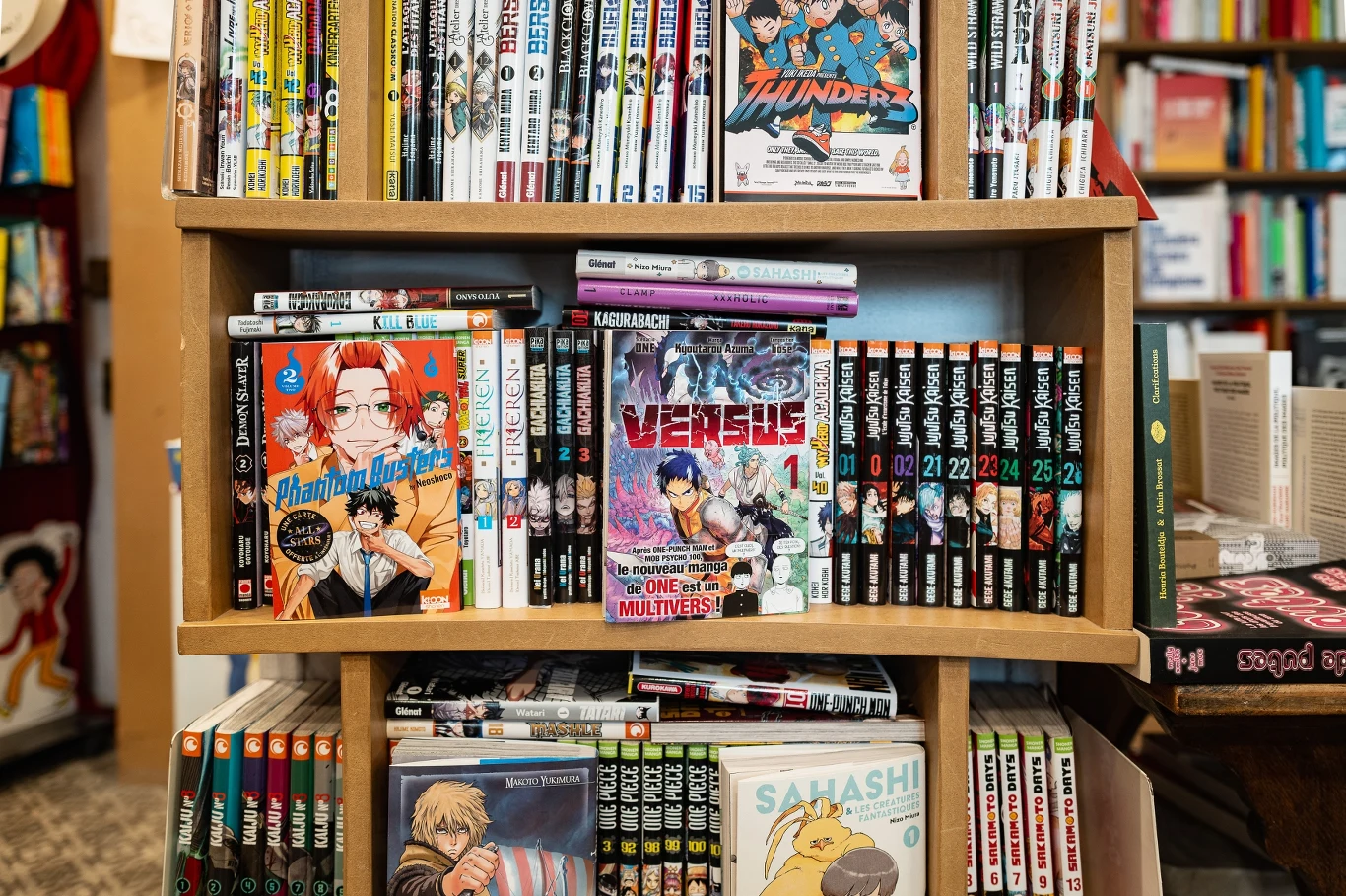 Regał wypełniony mangami i komiksami, na pierwszym planie wyeksponowane okładki różnych tytułów, z widocznymi kolorowymi ilustracjami i japońskimi napisami, w tle półki z książkami.