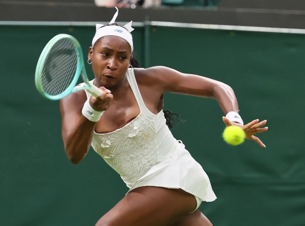 Coco Gauff na Wimbledonie Coco Gauff w białym stroju sportowym uderzająca piłkę rakietą podczas meczu na korcie trawiastym, w dynamicznej pozycji skupienia.