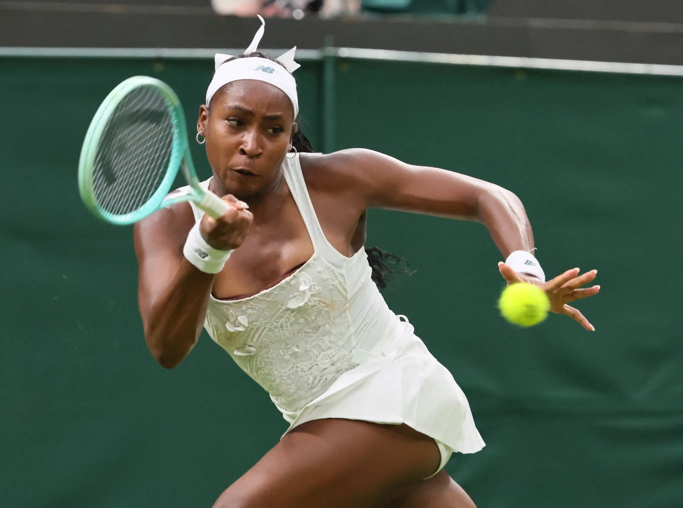 Coco Gauff w białym stroju sportowym uderzająca piłkę rakietą podczas meczu na korcie trawiastym, w dynamicznej pozycji skupienia.