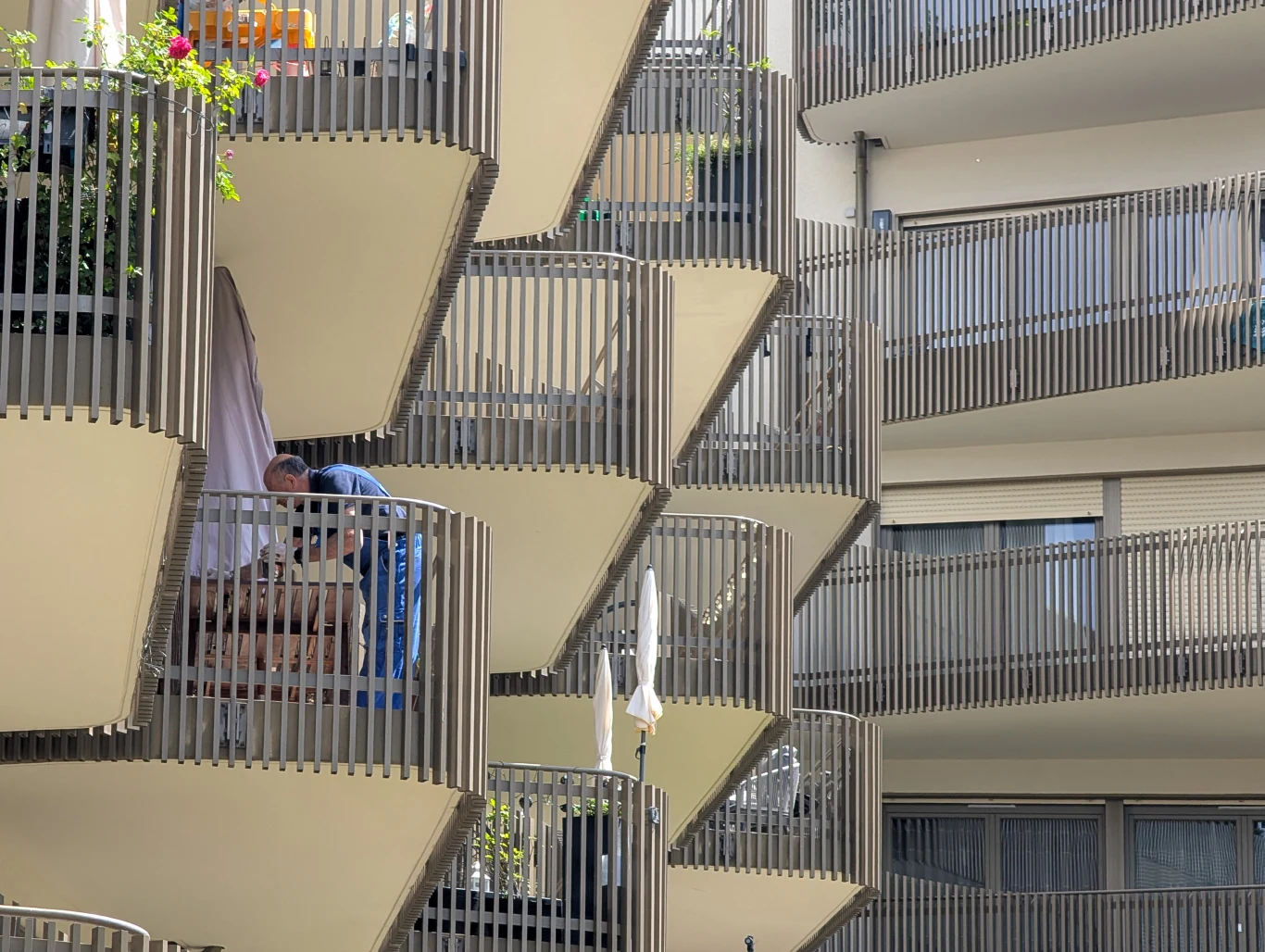 Według prawników deweloperzy stosują bezprawną praktykę. Każą płacić za powierzchnię, której nie powinno się wliczać w cenę Balkony nowoczesnego bloku mieszkalnego z charakterystycznymi balustradami ułożonymi w geometryczny wzór, osoba ustawiająca meble na jednym z balkonów.