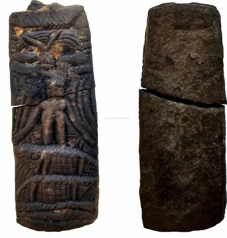Kamienny, wydłużony artefakt z wyrytymi motywami roślinnymi i zwierzęcymi oraz antropomorficzną postacią z wyciągniętymi ramionami, widoczny podział przez pęknięcie, drugi widok przedstawia tył bez zdobień.