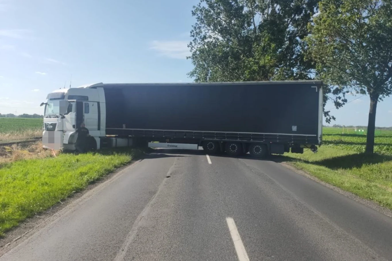 Kierowca postanowił zawrócić na drodze wojewódzkiej. Zablokował drogę. Tir stojący w poprzek wąskiej asfaltowej drogi blokując całkowicie przejazd, z jednej strony widoczne pole i rów, w tle zieleń oraz drzewa na poboczu.