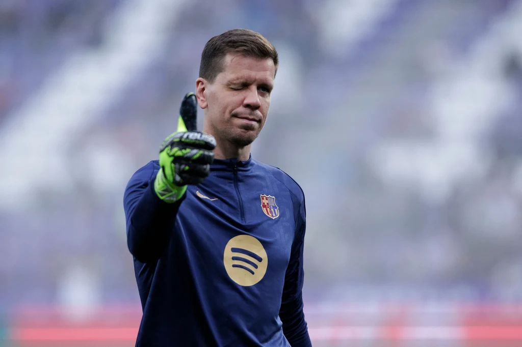 Wojciech Szczęsny Piłkarz w stroju bramkarskim pokazuje gest kciuka w górę, stoi na tle rozmytego stadionu. Ma na sobie granatową koszulkę z logotypem Spotify oraz rękawice bramkarskie.