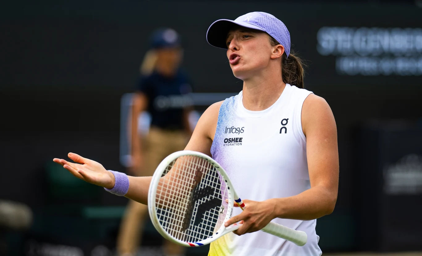 Iga Świątek Tenisistka wyrażająca emocje podczas meczu, ubrana w biały strój sportowy i fioletową czapkę, trzymająca rakietę tenisową, w tle rozmazana postać sędziego.