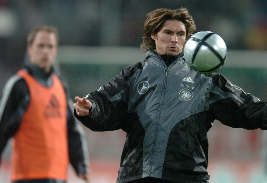 Thomas Brdarić w czasach kariery zawodniczej Piłkarz w kurtce treningowej z emblematami reprezentacji Niemiec kontroluje piłkę podczas treningu, w tle widoczny inny zawodnik w pomarańczowej kamizelce.