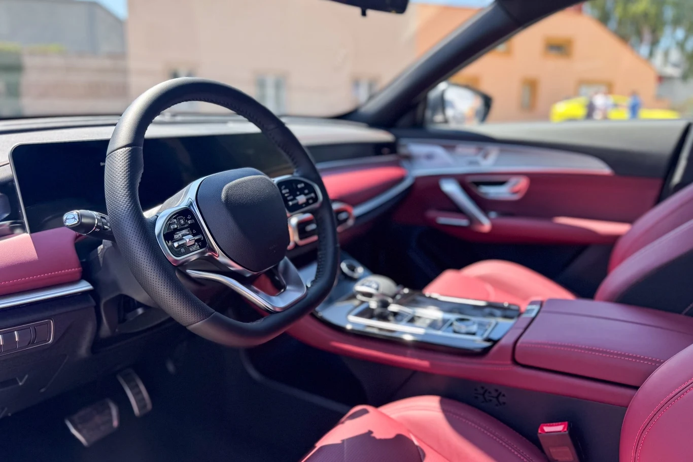 Luksusowe wnętrze nowoczesnego samochodu z czerwonymi skórzanymi siedzeniami, wielofunkcyjną kierownicą oraz dużym panelem dotykowym na konsoli środkowej.