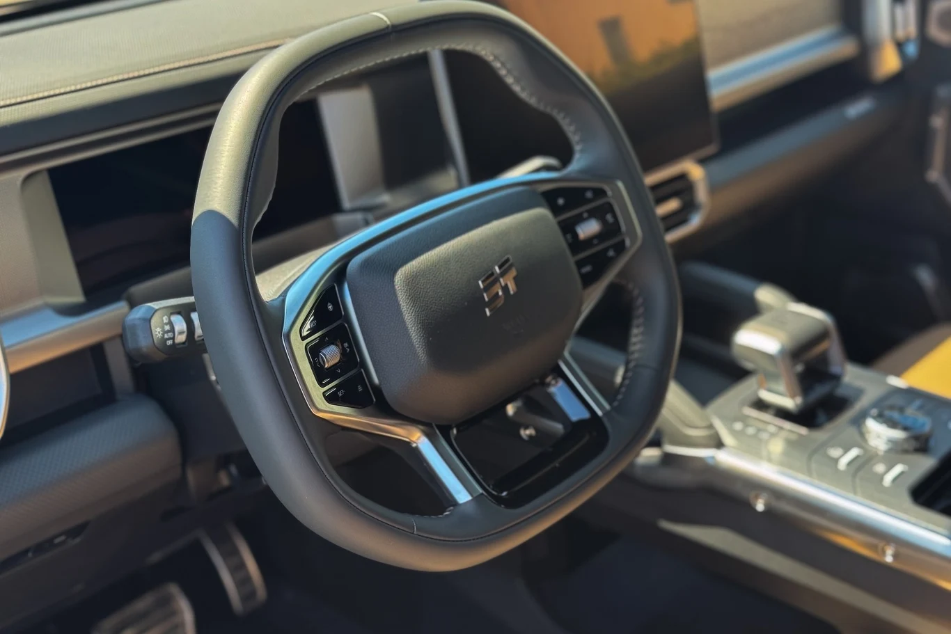 Nowoczesna kierownica samochodu z wieloma przyciskami sterującymi, panelem multimedialnym oraz elektroniczną dźwignią zmiany biegów w eleganckim, dobrze wyposażonym wnętrzu pojazdu.