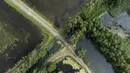 Szutrowa droga przecina akweny wodne i tereny podmokłe, otoczone zielenią oraz drzewami; widoczny układ geometryczny i kontrast między wodą a zielenią.