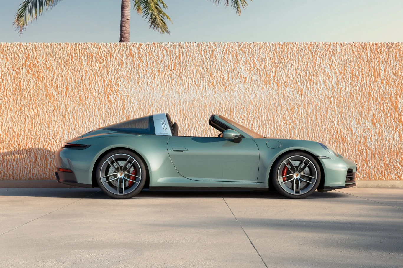 Porsche 911 Targa 4S Jasnozielony, sportowy kabriolet Porsche stoi zaparkowany na tle pomarańczowego muru, nad którym wystają palmy, a całość oświetla subtelne światło słoneczne.