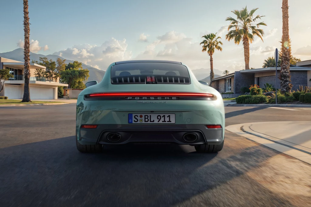 Porsche 911 Carrera 4S Jasnozielony sportowy samochód marki Porsche 911 widziany od tyłu, stojący na tle nowoczesnych domów, otoczony palmami i oświetlony ciepłym światłem słonecznym, w tle widoczne są góry.