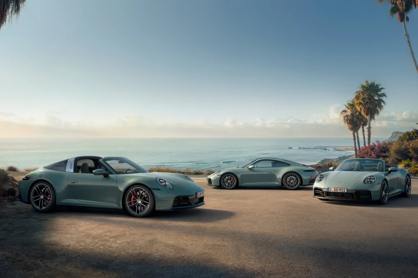 Porsche 911 Targa 4S, Carrera 4S oraz Carrera 4S Cabriolet Trzy sportowe samochody tej samej marki zaparkowane w słonecznym miejscu przy wybrzeżu, w tle morze i palmy, widoczny spokojny krajobraz oraz bezchmurne niebo.