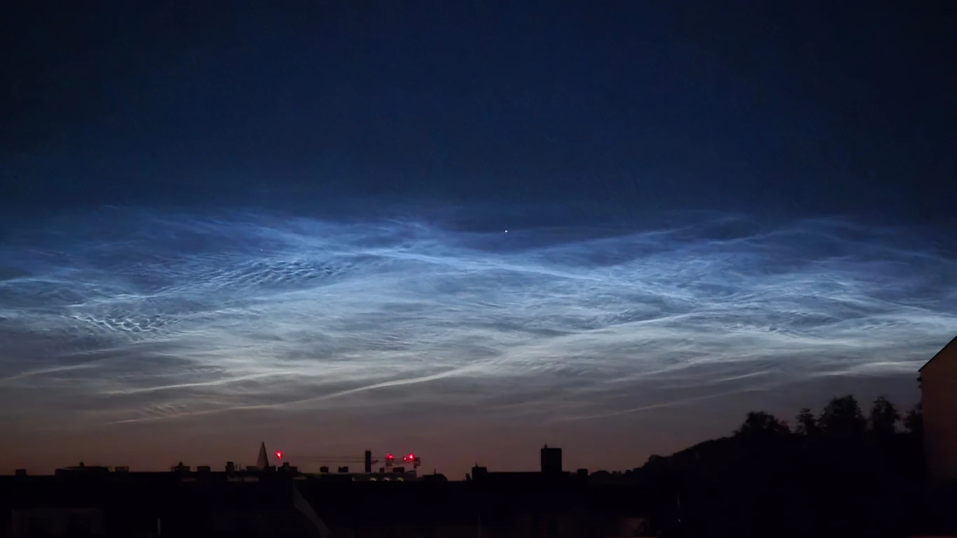 To zjawisko pojawia się tylko latem. Wczoraj zachwyciło Polaków! Nocne, jasne chmury świecące nad ciemnym horyzontem miasta, z widocznymi zarysami budynków oraz rozproszonymi światłami miejskimi poniżej.