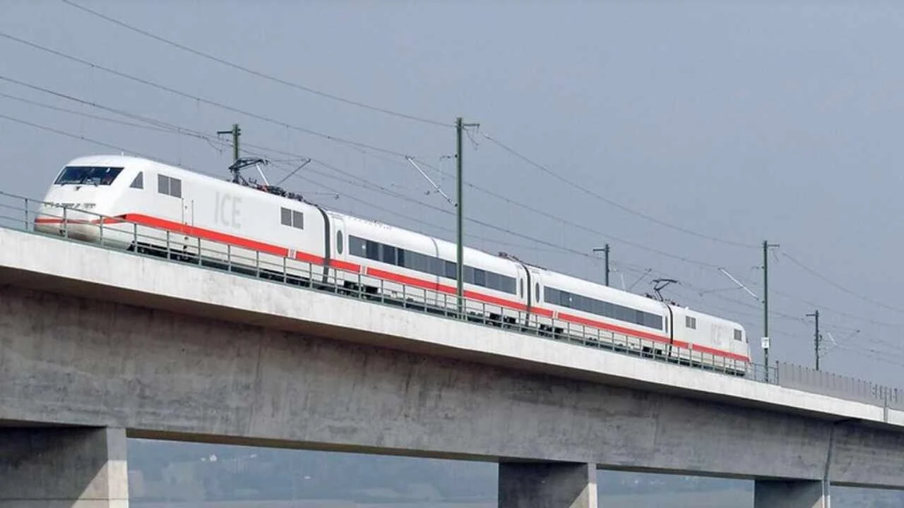 Pociąg ICE rozpędzony do ponad 400 km/h. Nowy rekord w Niemczech. Nowoczesny pociąg dużych prędkości ICE jadący po betonowym wiadukcie, otoczony przez słupy trakcyjne i prowadzący przez otwartą przestrzeń.