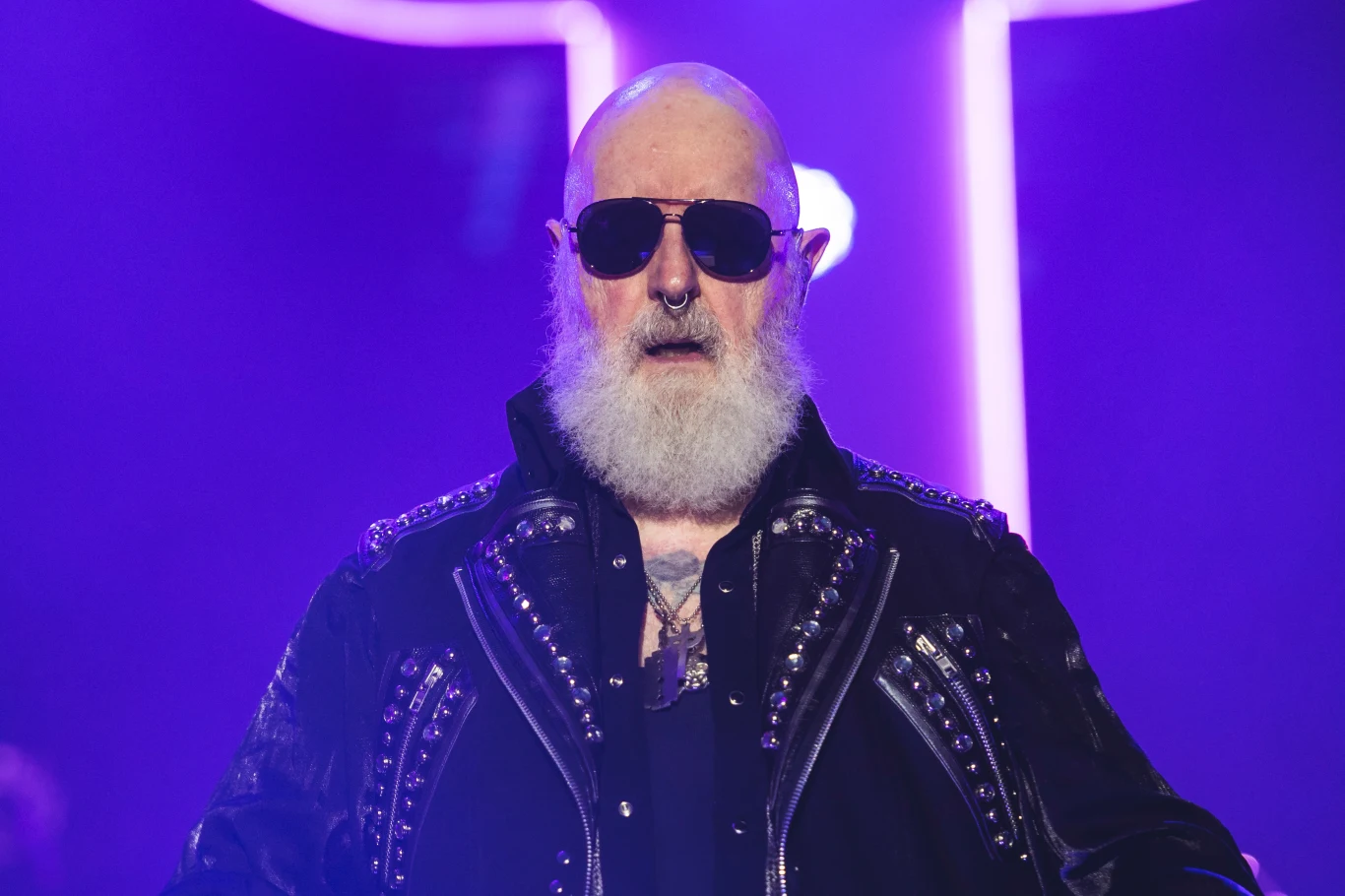 Rob Halford razem z grupą Judas Priest oddał hołd Black Sabbath Starszy mężczyzna z białą brodą i wąsami, ubrany w czarną, skórzaną kurtkę z ćwiekami, noszący okulary przeciwsłoneczne i kolczyk w nosie, stoi na tle fioletowego światła scenicznego.