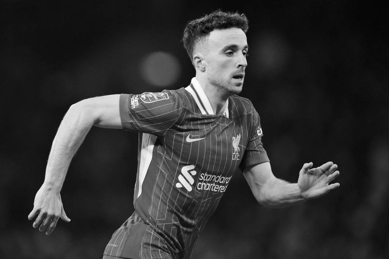Piłkarz w stroju sportowym Liverpool FC podczas biegu po murawie boiska, z widocznym logotypem sponsora na koszulce.