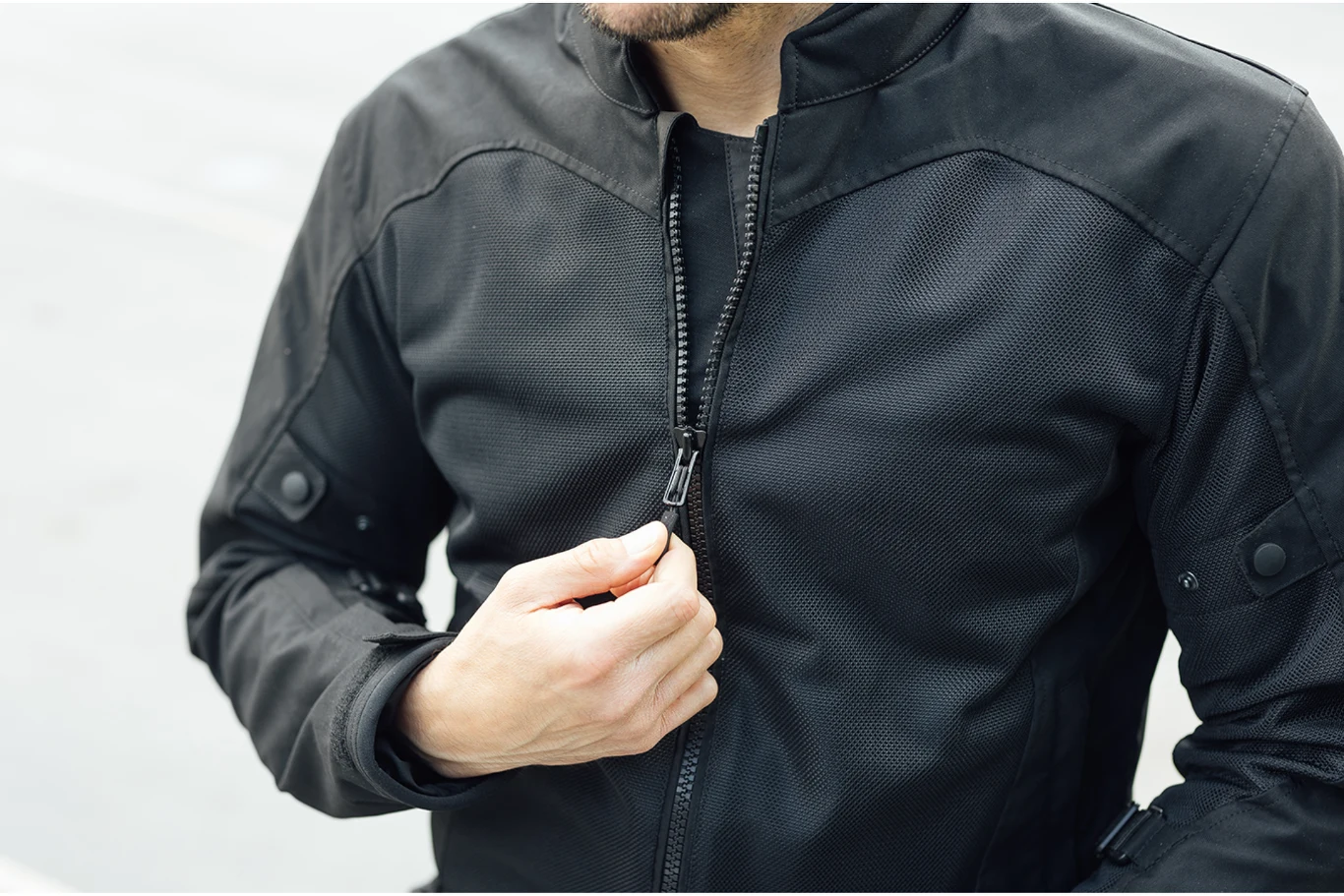 Mężczyzna w czarnej kurtce sportowej zapinający suwak, widoczne tylko górna część sylwetki i ręce.