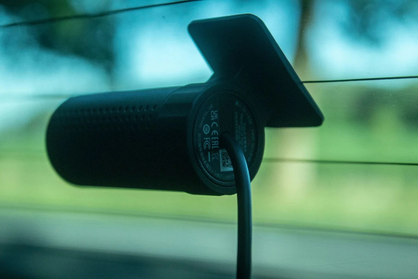 Kamera samochodowa zamocowana na tylnej szybie pojazdu, z widocznym przewodem zasilającym, w tle rozmazany krajobraz za szybą.