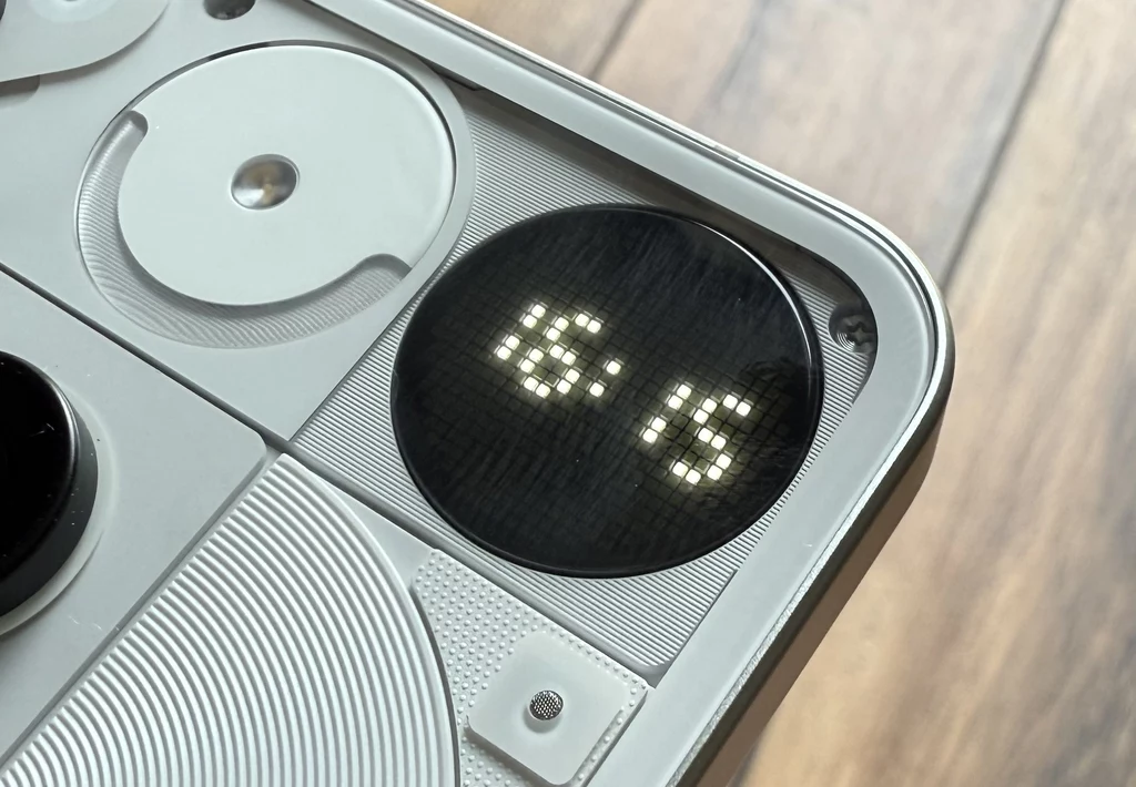 Glyph Matrix z Nothing Phone 3, Zbliżenie na tylną obudowę nowoczesnego smartfona z okrągłym ekranem wyświetlającym godzinę 16:16, widoczne elementy konstrukcyjne i designerskie detale obudowy.