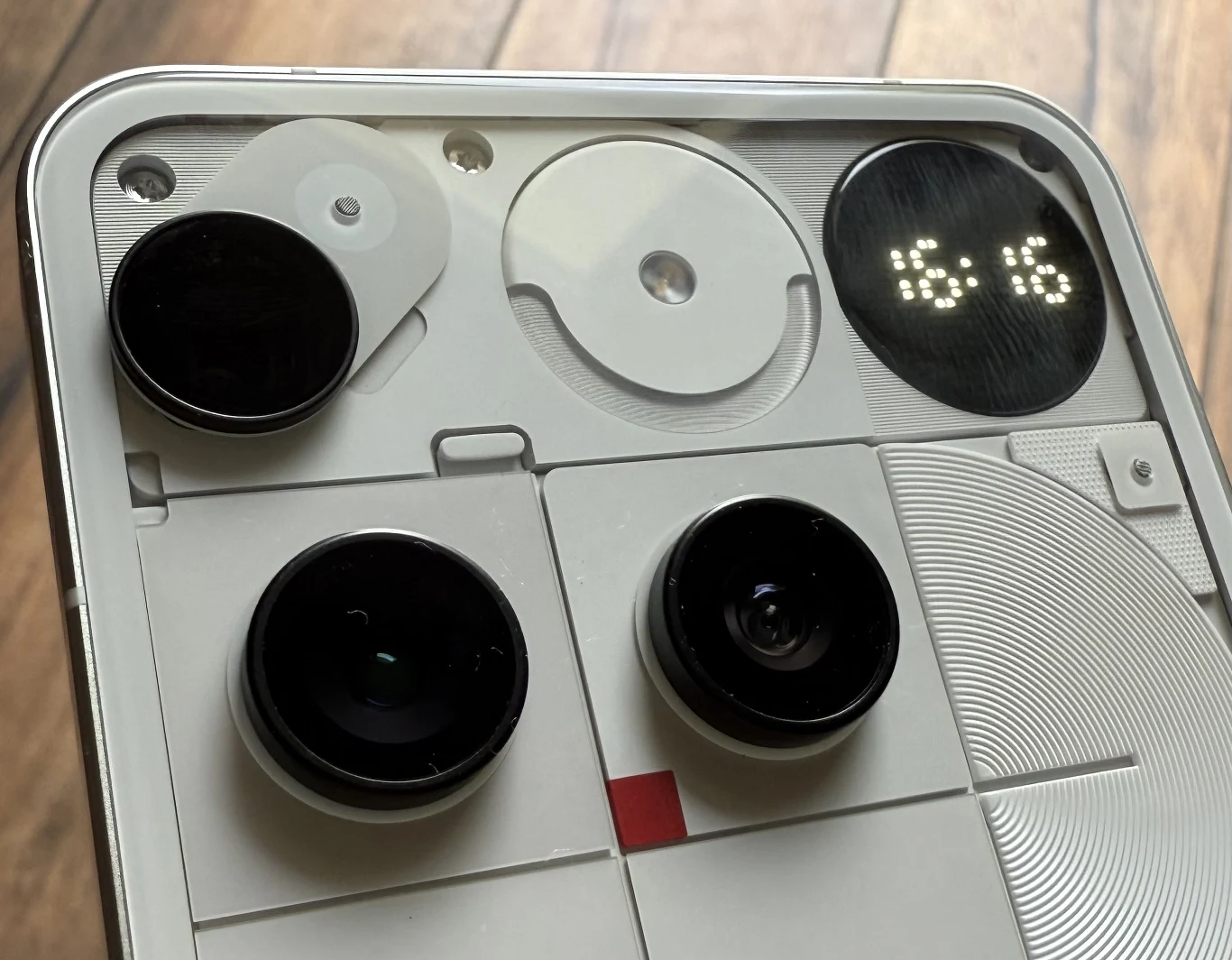 Zbliżenie na tylną obudowę nowoczesnego smartfona z widocznymi obiektywami aparatów, lampą LED oraz minimalistycznym, technicznym wzornictwem z geometrycznymi elementami i cyfrowym wyświetlaczem LED pokazującym godzinę.