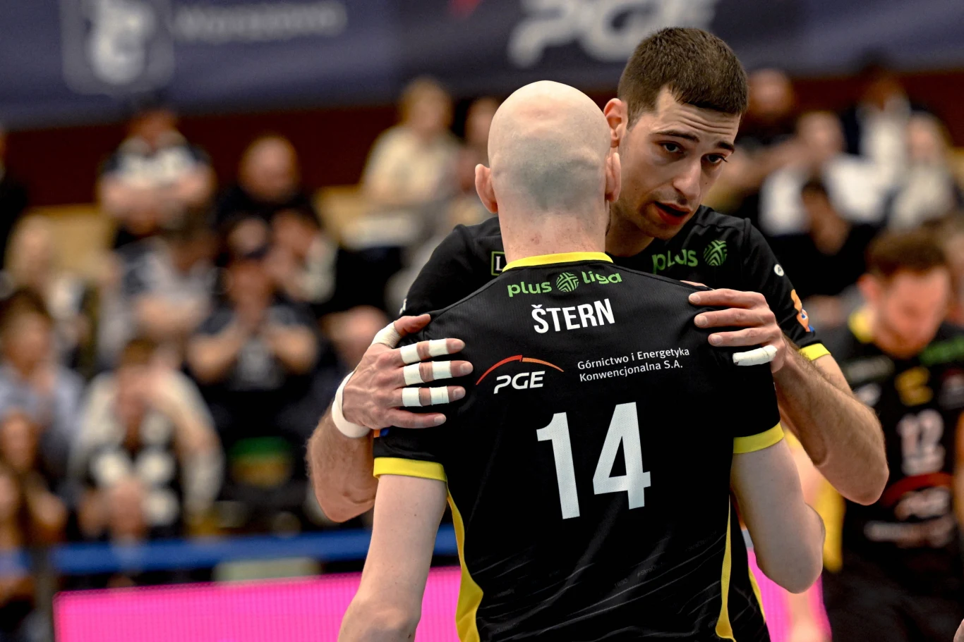 Pavle Perić i Żiga Stern podjęli zaskakującą decyzję. Wprost z PlusLigi przenoszą się do Rosji Dwóch siatkarzy ubranych w czarne koszulki z logo sponsorów na plecach, jeden z zawodników trzyma drugiego za ramiona, atmosfera skupienia oraz współpracy, rozmyte postacie i trybuny w tle.