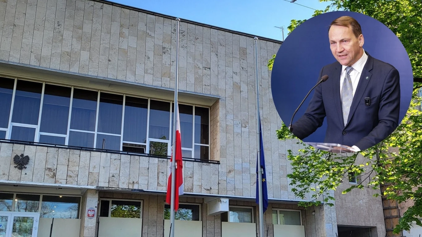 Atak w Kijowie. Sikorski: Ucierpiał budynek naszej ambasady Budynek z kamienną elewacją, przed którym znajdują się dwie flagi na masztach, jedna z nich opuszczona do połowy, z widocznym godłem Polski na fasadzie, a w okrągłym kadrze po prawej stronie uśmiechnięty mężczyzna w garniturze stojący przy mównicy.