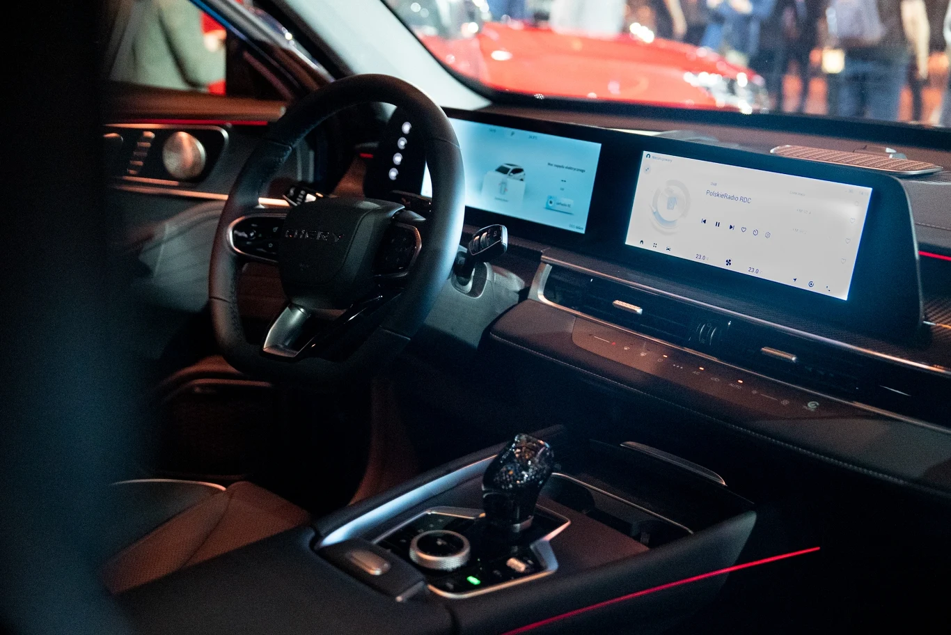 Luksusowy kokpit nowoczesnego samochodu z dużym panoramicznym ekranem dotykowym na desce rozdzielczej, sportową kierownicą i zaawansowaną konsolą środkową, wnętrze wykończone eleganckimi materiałami z podświetleniem LED.