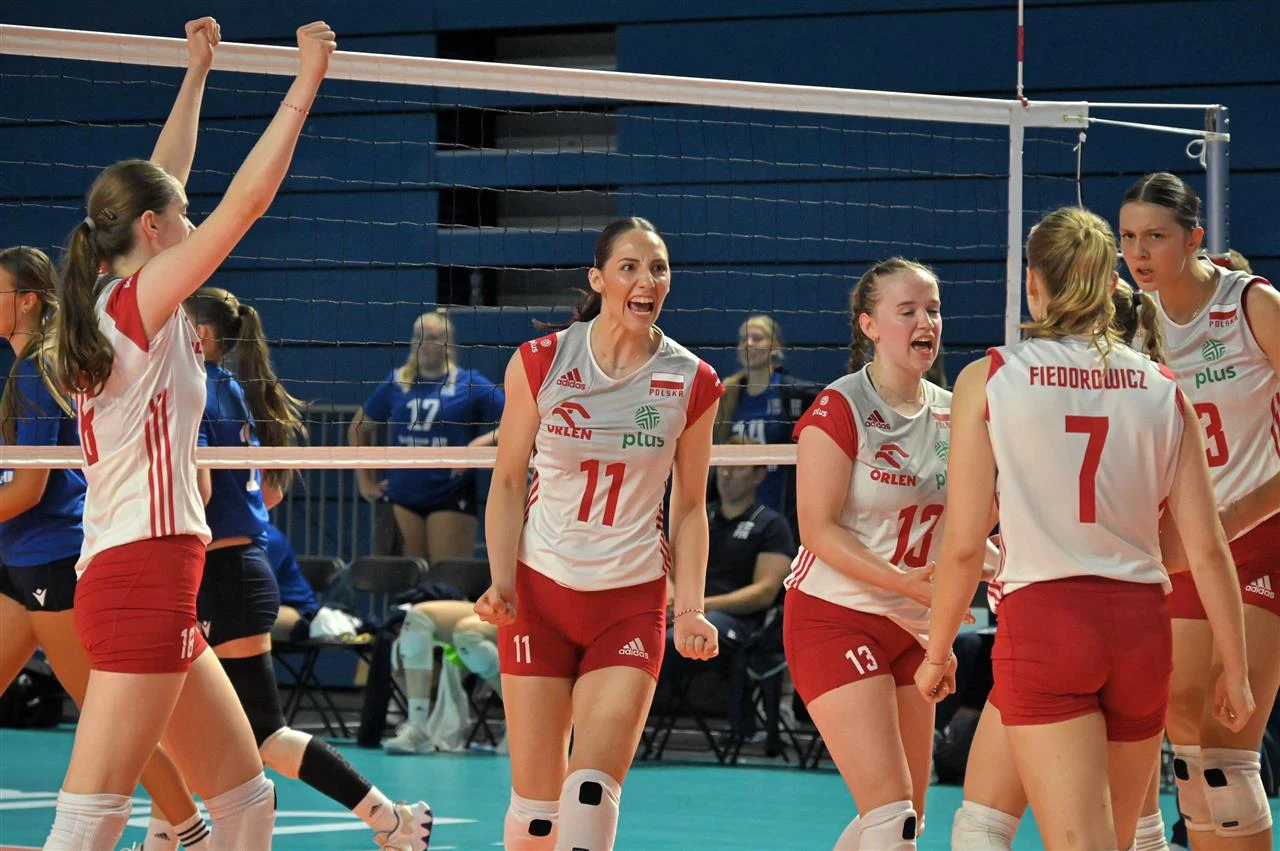 Polskie siatkarki w czasie ubiegłorocznych mistrzostw Europy do lat 20 Grupa siatkarek w biało-czerwonych strojach drużyny narodowej świętuje zdobyty punkt na boisku, otaczając centralną postać z numerem 11, która wyraża entuzjazm i radość, w tle przeciwniczki w niebieskich strojach.