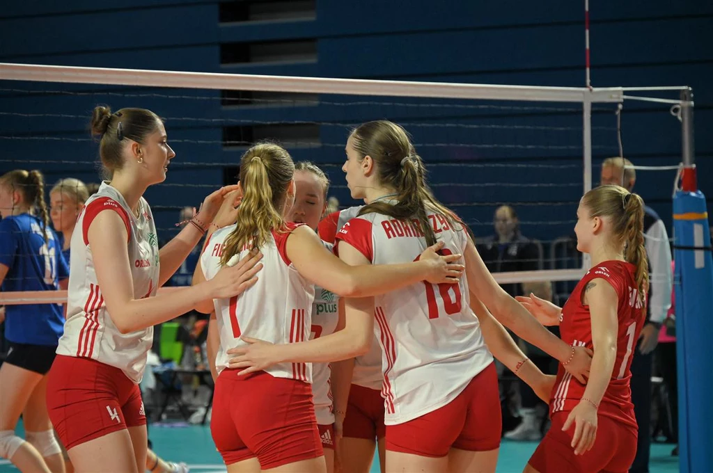 Polskie siatkarki w czasie ME U-20 2024 Zawodniczki drużyny siatkarskiej w biało-czerwonych strojach celebrują zdobyty punkt na boisku, wykonując gesty radości i wzajemnie się obejmując, w tle widać siatkę, przeciwniczki oraz sędziów.