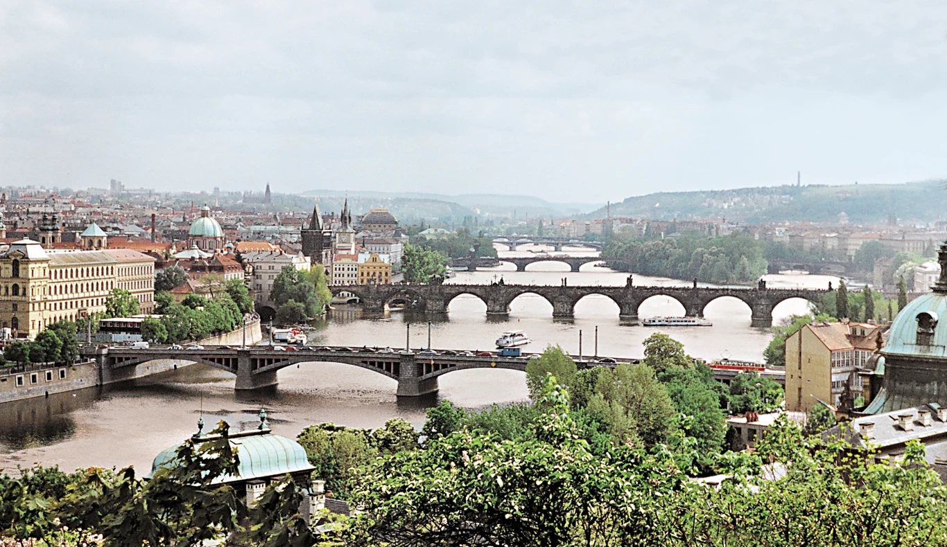 Blackout w Czechach. Czeska Praga, zdjęcie ilustracyjne Panorama miasta z licznymi mostami nad rzeką, gęsta zabudowa, charakterystyczne zabytki i kopuły, zielone tereny w pobliżu wody oraz łodzie płynące po rzece.