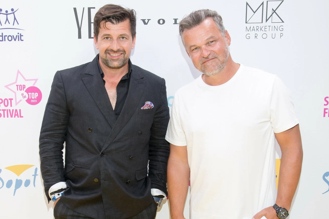 Patryk Mikiciuk i Adam Kornacki zaprzeczają stawianym im zarzutom Dwóch mężczyzn pozuje na tle ścianki z logo różnych firm i wydarzeń, jeden ubrany w czarny garnitur, drugi w białą koszulkę.