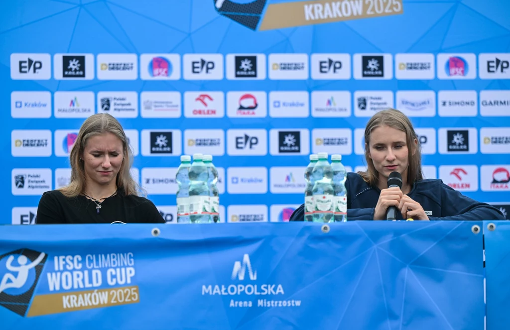 Natalia Kałucka, Aleksandra Kałucka Dwie kobiety siedzące za stołem podczas konferencji prasowej, na tle ściany z logotypami sponsorów i organizatorów IFSC Climbing World Cup Kraków 2025; jedna z nich mówi do mikrofonu, na stole butelki z wodą mineralną.