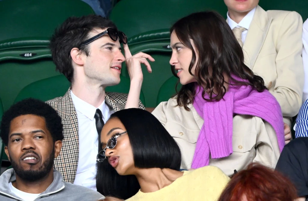 Tom Sturridge i Alexa Chung na Wimbledonie w 2023 r. Kilka osób siedzi na trybunach, dwoje z nich patrzy sobie głęboko w oczy i rozmawia, pozostałe osoby skupione są na otaczającym ich wydarzeniu.