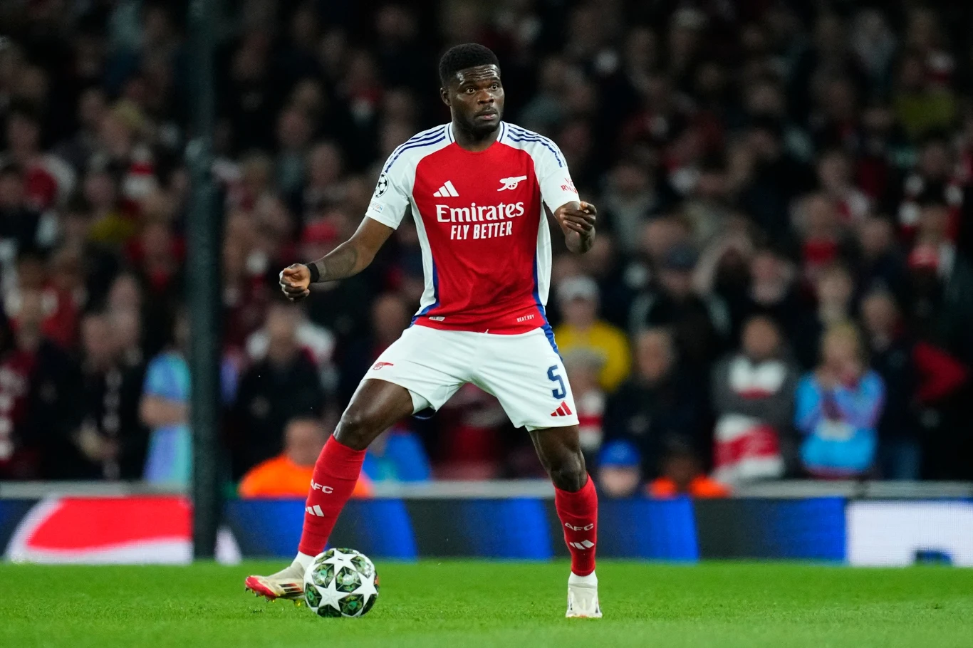 Zawodnik w czerwono-białym stroju piłkarskim drużyny Arsenal kontroluje piłkę podczas meczu na stadionie, w tle rozmazana publiczność.