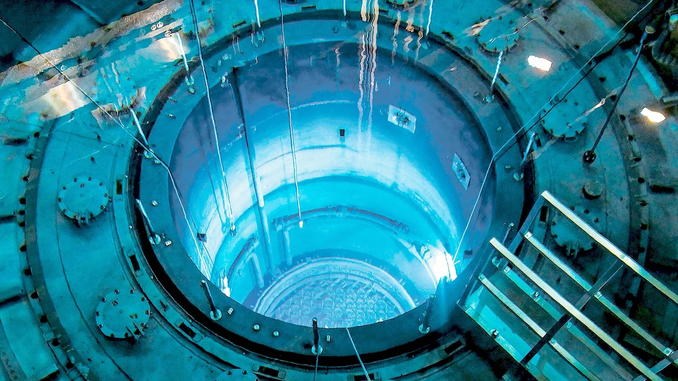 Bill Gates buduje pierwszą w historii prywatną elektrownię atomową centralny otwór reaktora jądrowego otoczony metalowymi elementami, głęboka niebieska poświata to efekt promieniowania Czerenkowa, widoczne konstrukcje techniczne oraz metalowa barierka po bokach