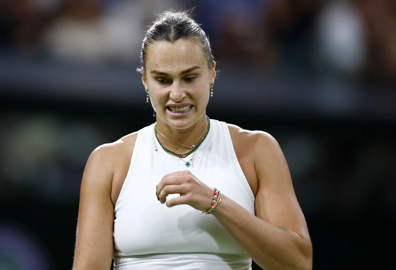 Zbliżenie kobiety w sportowym stroju na korcie tenisowym z widoczną napiętą mimiką twarzy i splecionymi rękami, tło rozmyte, skupienie na emocjach zawodniczki.