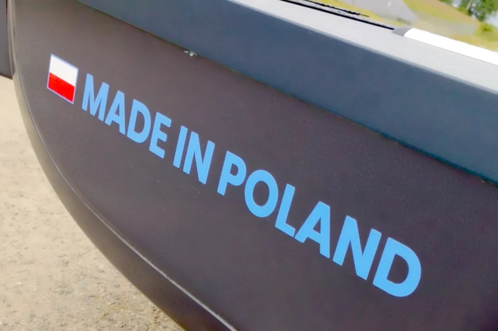 Samochód od podstaw został zaprojektowany w Polsce Napis 'MADE IN POLAND' namalowany na ciemnej powierzchni obok polskiej flagi, litery są w jasnoniebieskim kolorze.