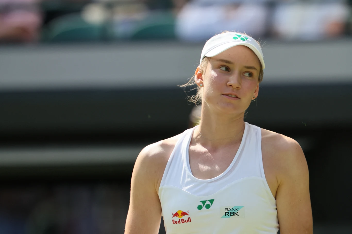 Jelena Rybakina rywalizowała z Clarą Tauson o awans do czwartej rundy Wimbledonu Kobieta w sportowym stroju tenisowym i białej czapce z daszkiem stoi na korcie tenisowym, w tle rozmyte trybuny. Na jej koszulce widoczne są loga sponsorów.