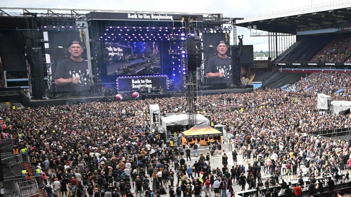 Pożegnalny koncert Black Sabbath Tłum ludzi zgromadzonych na stadionie podczas dużego koncertu, scena z efektami świetlnymi oraz ekranami z wizerunkiem prowadzącego, nad głowami uczestników rozpościera się otwarta przestrzeń stadionu.