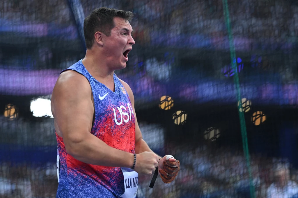 Rudy Winkler Sportowiec w stroju reprezentacji USA w trakcie zawodów lekkoatletycznych, wyraża emocje, najprawdopodobniej po wykonaniu rzutu, w tle rozmazana publiczność stadionowa.