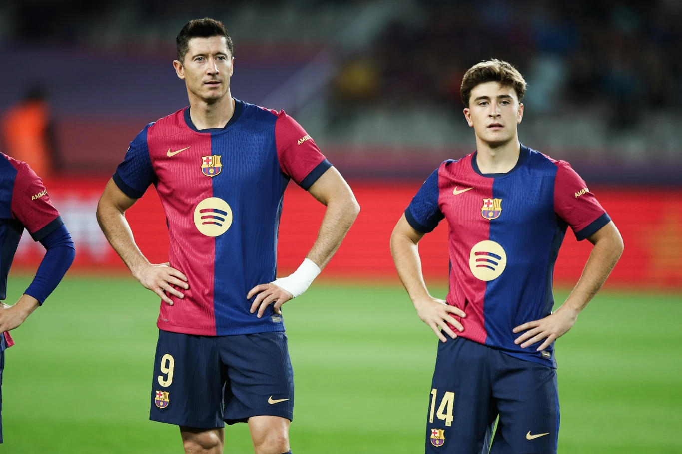 Robert Lewandowski, Pablo Torre Dwóch piłkarzy klubu FC Barcelona w oficjalnych strojach drużyny, obaj z rękami opartymi na biodrach, stojący na murawie stadionu.
