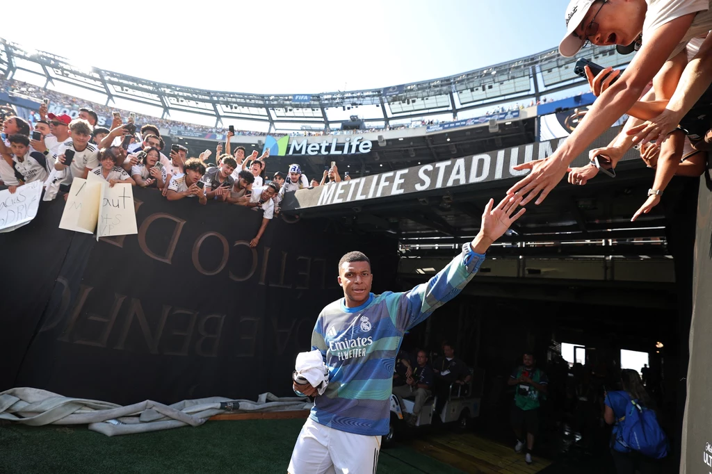 Kylian Mbappe znowu w wielkiej grze Piłkarz w stroju klubowym opuszcza tunel stadionu MetLife, machając do licznie zgromadzonych kibiców, którzy wyciągają do niego ręce i trzymają transparenty.