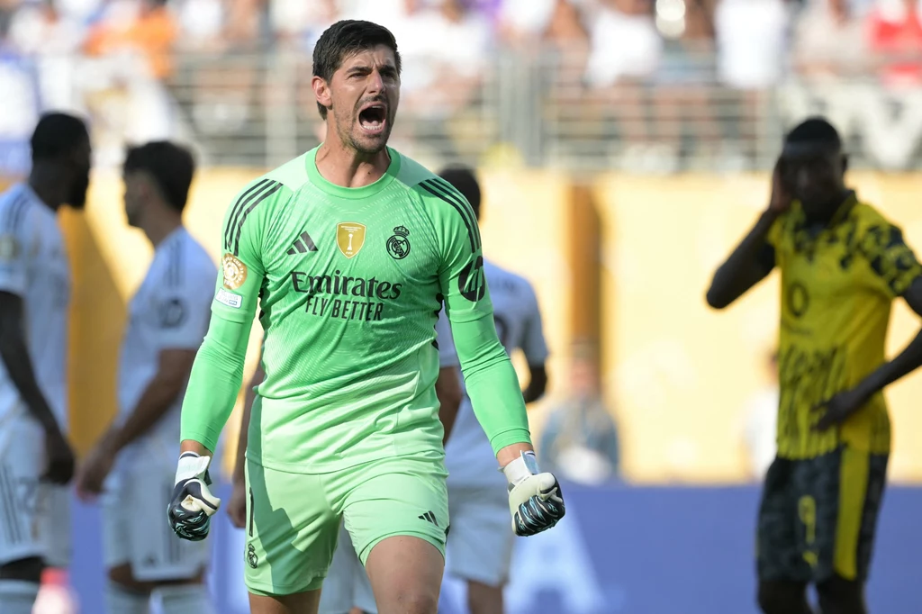 Thibaut Courtois skapitulował dwukrotnie, ale po ostatnim gwizdku miał powody do satysfakcji Bramkarz w zielonym stroju sportowym z logo Realu Madryt wyraża silne emocje, trzymając zaciśnięte pięści, w tle piłkarze obu drużyn na boisku, atmosfera pełna napięcia typowa dla meczu piłkarskiego.