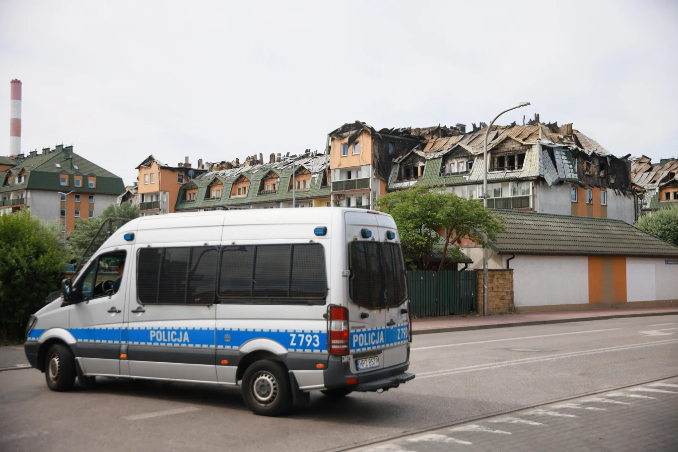 Część mieszkańców może wejść do spalonego bloku w Ząbkach Policyjny radiowóz stoi na ulicy obok budynku mieszkalnego o spalonym dachu oraz zniszczonymi oknami, w tle widoczny komin przemysłowy.